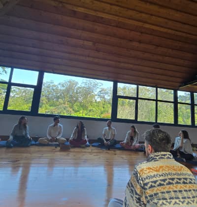 The group sitting in a circle in a wooden hall with tall windows